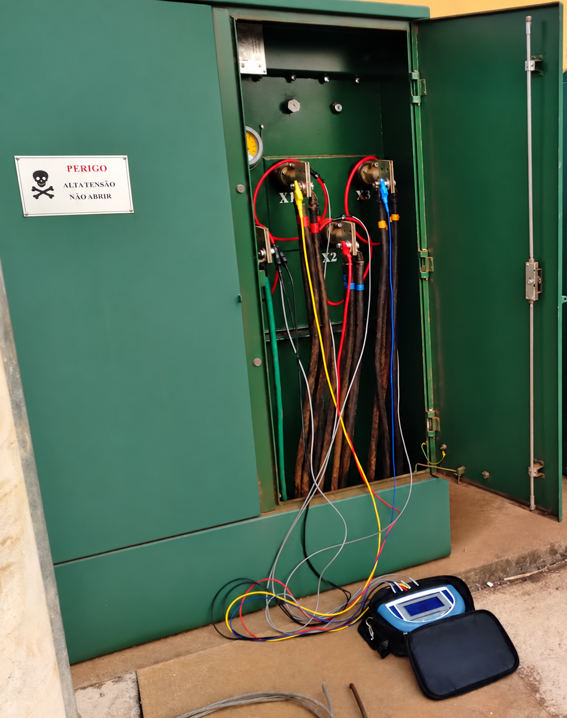 Instrumento de medição em estojo conectado por cabos a uma instalação elétrica aberta.
